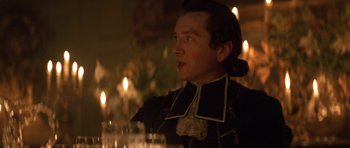 Movie still from “Ridicule” (1996), directed by Patrice Leconte – A man in a black suit sitting in front of candles; Close Up shot, Over the shoulder angle