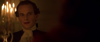 Movie still from “Ridicule” (1996), directed by Patrice Leconte – A man in a red shirt is smiling for the camera; Close Up shot, Over the shoulder angle