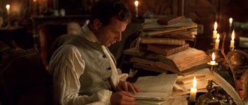 Movie still from “Ridicule” (1996), directed by Patrice Leconte – A man sitting in front of a stack of books; Medium shot, High angle