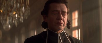 Movie still from “Ridicule” (1996), directed by Patrice Leconte – A man with long brown hair wearing a black shirt; Close Up shot, Low angle