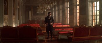 Movie still from “Ridicule” (1996), directed by Patrice Leconte – A man standing in front of a room filled with red chairs; Wide shot, Low angle