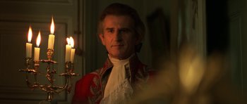 Movie still from “Ridicule” (1996), directed by Patrice Leconte – A man in a red and white jacket is looking at the camera; Close Up shot, Over the shoulder angle