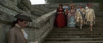 Movie still from “Ridicule” (1996), directed by Patrice Leconte – A group of people dressed in period costumes walking down a set of stairs; Wide shot, Low angle