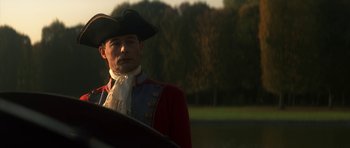 Movie still from “Ridicule” (1996), directed by Patrice Leconte – A man in a red coat and a black hat; Medium shot, Low angle