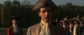 Movie still from “Ridicule” (1996), directed by Patrice Leconte – A man wearing a hat and a suit; Close Up shot, Over the shoulder angle