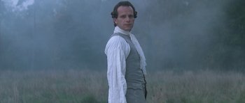 Movie still from “Ridicule” (1996), directed by Patrice Leconte – A man standing in a field wearing a white shirt and tie; Medium shot, Low angle