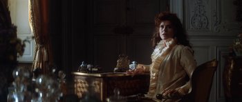 Movie still from “Ridicule” (1996), directed by Patrice Leconte – A woman sitting in front of a table; Medium shot, Over the shoulder angle