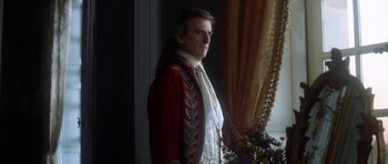Movie still from “Ridicule” (1996), directed by Patrice Leconte – A man in a red and white outfit standing in front of a window; Medium shot, Over the shoulder angle