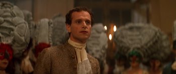 Movie still from “Ridicule” (1996), directed by Patrice Leconte – A man wearing a suit and tie standing in front of candles; Close Up shot, Over the shoulder angle