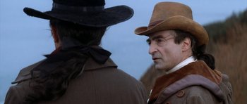 Movie still from “Ridicule” (1996), directed by Patrice Leconte – A man in a cowboy hat and a man in a brown jacket; Close Up shot, Over the shoulder angle