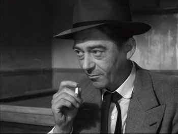 Movie still from “Rififi” (1955), directed by Jules Dassin – A black and white photo of a man smoking a cigarette; Close Up shot, High angle
