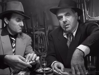 Movie still from “Rififi” (1955), directed by Jules Dassin – Two men sitting at a table in front of drinks; Medium shot, Low angle