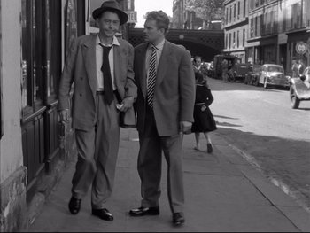 Movie still from “Rififi” (1955), directed by Jules Dassin – Two men are walking down the sidewalk of a city street; Medium shot, High angle