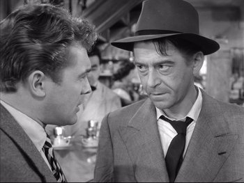 Movie still from “Rififi” (1955), directed by Jules Dassin – A man in a suit and hat talking to another man in a suit; Close Up shot, Over the shoulder angle