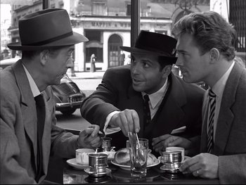 Movie still from “Rififi” (1955), directed by Jules Dassin – A group of men sitting at a table with food; Medium shot, Over the shoulder angle