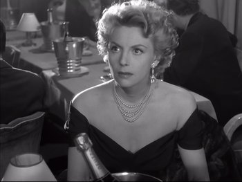 Movie still from “Rififi” (1955), directed by Jules Dassin – An old photo of a woman in a black dress with a bottle of champagne; Close Up shot, Over the shoulder angle