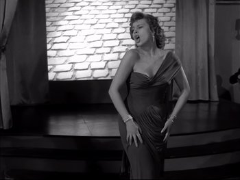 Movie still from “Rififi” (1955), directed by Jules Dassin – A black and white photo of a woman singing; Medium shot, Low angle