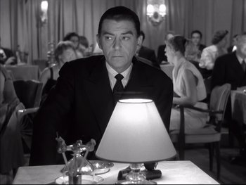 Movie still from “Rififi” (1955), directed by Jules Dassin – A black and white photo of a man sitting at a table; Medium shot, Low angle