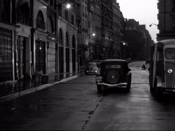Movie still from “Rififi” (1955), directed by Jules Dassin – An old car is parked on the side of the street; Wide shot, High angle