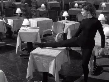 Movie still from “Rififi” (1955), directed by Jules Dassin – A woman stretching her leg on a table in a restaurant; Wide shot, High angle
