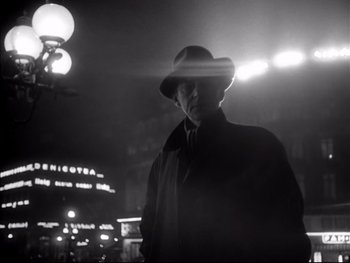 Movie still from “Rififi” (1955), directed by Jules Dassin – A black and white photo of a man wearing a hat; Medium shot, Low angle