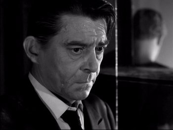 Movie still from “Rififi” (1955), directed by Jules Dassin – Black and white photograph of a man in a suit and tie; Close Up shot, Low angle