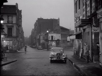 Movie still from “Rififi” (1955), directed by Jules Dassin – An old car parked on the side of the street; Extreme Wide shot, High angle