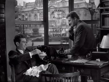 Movie still from “Rififi” (1955), directed by Jules Dassin – Two men sitting at a table with a black cat; Medium shot, High angle