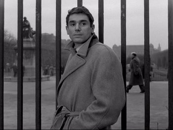 Movie still from “Rififi” (1955), directed by Jules Dassin – A black and white photo of a man standing in front of a fence; Medium shot, Low angle