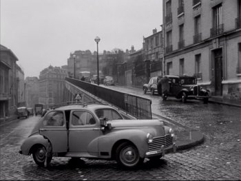 Movie still from “Rififi” (1955), directed by Jules Dassin – An old car parked on the side of the street; Wide shot, High angle