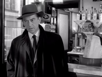 Movie still from “Rififi” (1955), directed by Jules Dassin – A black and white photo of a man wearing a hat; Medium shot, Over the shoulder angle