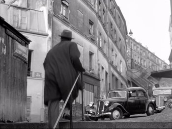 Movie still from “Rififi” (1955), directed by Jules Dassin – An older man is standing on the sidewalk with a cane; Wide shot, High angle