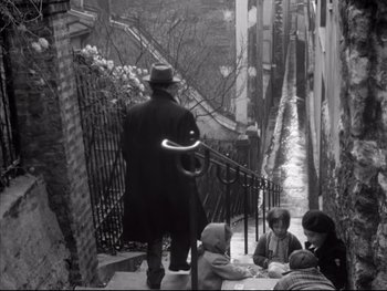 Movie still from “Rififi” (1955), directed by Jules Dassin – A man walking down a street with a cane; Wide shot, High angle