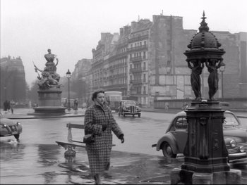 Movie still from “Rififi” (1955), directed by Jules Dassin – An old photo of a woman walking in the rain; Wide shot, High angle