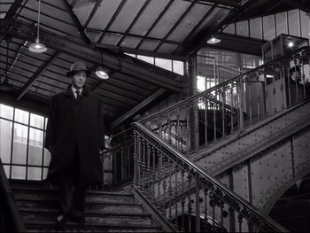 Movie still from “Rififi” (1955), directed by Jules Dassin – A black and white photo of a man walking up a set of stairs; Wide shot, Low angle
