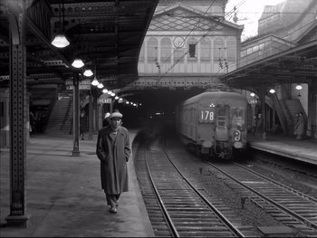 Movie still from “Rififi” (1955), directed by Jules Dassin – A man walking on a train platform next to a train; Wide shot, Low angle