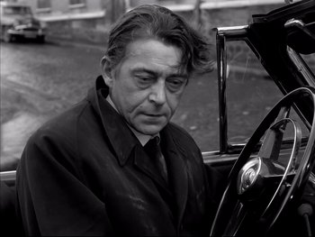 Movie still from “Rififi” (1955), directed by Jules Dassin – An older man wearing a black coat and tie; Close Up shot, High angle