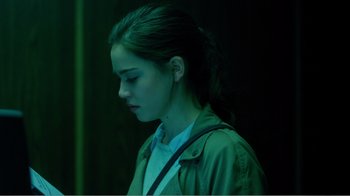 Movie still from “Rings” (2017), directed by F. Javier Gutiérrez – A young woman is standing in a dark room; Close Up shot, Over the shoulder angle
