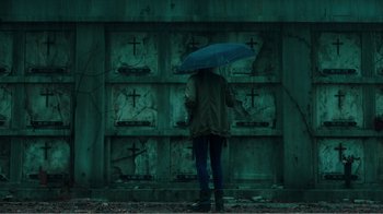 Movie still from “Rings” (2017), directed by F. Javier Gutiérrez – A person holding an umbrella standing in front of crosses; Wide shot, Low angle