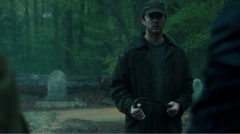 Movie still from “Rings” (2017), directed by F. Javier Gutiérrez – A man wearing a hat and a jacket in the woods; Medium shot, Over the shoulder angle