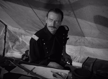 Movie still from “Rio Grande” (1950), directed by John Ford – A black and white photo of a man sitting at a table; Close Up shot, Low angle