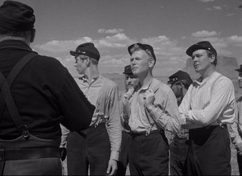 Movie still from “Rio Grande” (1950), directed by John Ford – A black and white photo of a group of men standing together; Medium shot, Low angle