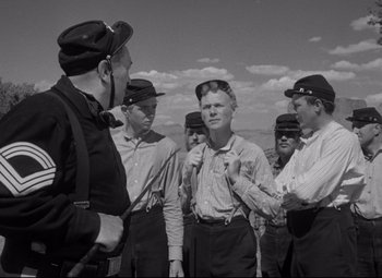 Movie still from “Rio Grande” (1950), directed by John Ford – A black and white photo of a group of men in hats; Medium shot, Over the shoulder angle