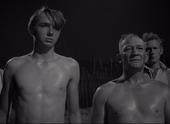 Movie still from “Rio Grande” (1950), directed by John Ford – A man and a young boy standing next to each other; Medium shot, Low angle