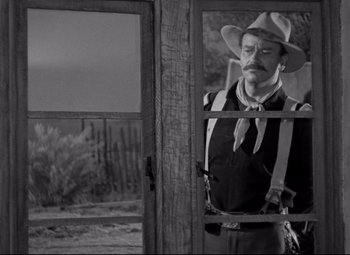 Movie still from “Rio Grande” (1950), directed by John Ford – A man wearing a cowboy hat looking out of a window; Medium shot, Over the shoulder angle