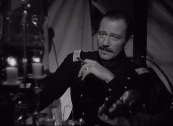 Movie still from “Rio Grande” (1950), directed by John Ford – A black and white photo of a man smoking a cigarette; Close Up shot, Over the shoulder angle