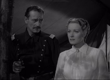 Movie still from “Rio Grande” (1950), directed by John Ford – A man and a woman standing next to each other; Medium shot, Low angle