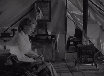 Movie still from “Rio Grande” (1950), directed by John Ford – A woman sitting on a chair next to a man in a tent; Wide shot, High angle