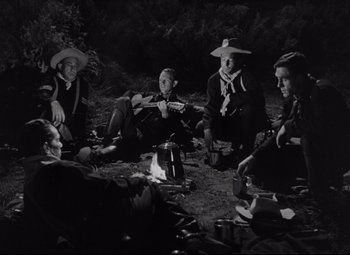 Movie still from “Rio Grande” (1950), directed by John Ford – A group of people sitting around a campfire at night; Medium shot, High angle