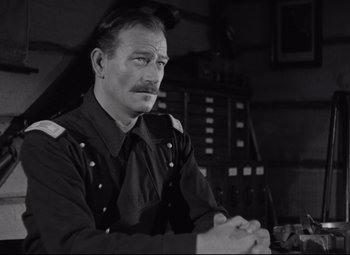 Movie still from “Rio Grande” (1950), directed by John Ford – A man in uniform sitting in front of a desk; Medium shot, Over the shoulder angle